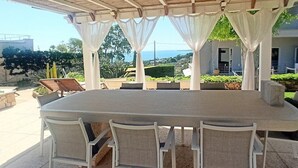 An outdoor covered patio with a large table and chairs, surrounded by white curtains, overlooking a scenic view.