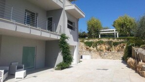 A modern two-story building with a balcony, a stone retaining wall, and a clear blue sky.