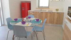 A modern kitchen with a dining table set for four, featuring blue chairs and purple bowls.