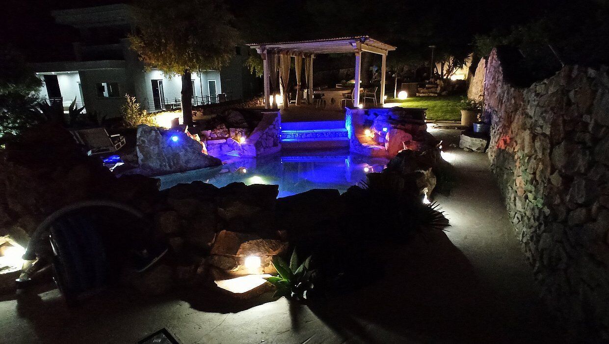 A nighttime outdoor swimming pool area with a gazebo, stone steps, and ambient lighting.