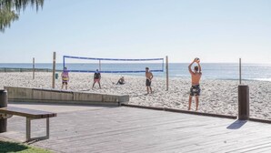Partido de voleibol de playa sobre una terraza de madera con una red, sillas y un cubo de basura.
