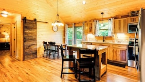 Interior de una cabaña de madera con cocina, comedor y una amplia puerta de madera.