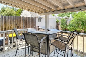 A covered patio with a table and four chairs, a wooden fence, and a white building in the background. - Miracle Mile Stay: Classic Stockton Home w/ Yard! (Stockton)