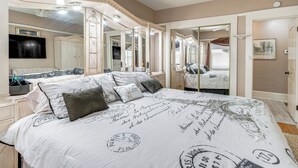 Ein Schlafzimmer mit einem großen Bett, mehreren Spiegeln, einem Schminktisch mit Spiegel und einem Fernseher an der Wand.