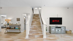 A staircase leading to a second floor, a television mounted on the wall, and a console table with books and decorative items.