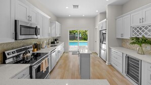 A modern kitchen with white cabinetry, stainless steel appliances, and a view of a swimming pool.