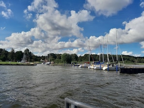 Un port de plaisance où sont amarrés plusieurs voiliers, l’eau est calme et le ciel est dégagé, avec quelques nuages.