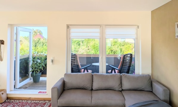 A living room with a sofa, a sliding glass door leading to an outdoor patio with a table and chairs.