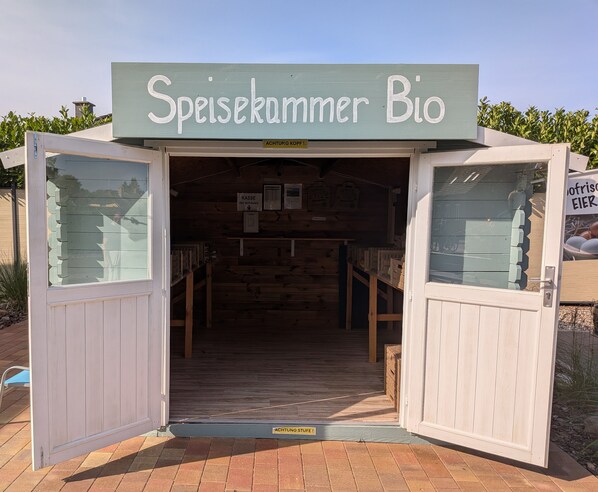 Une structure en bois avec une enseigne indiquant « Speisekammer Bio » et des portes ouvertes donnant sur l’intérieur.