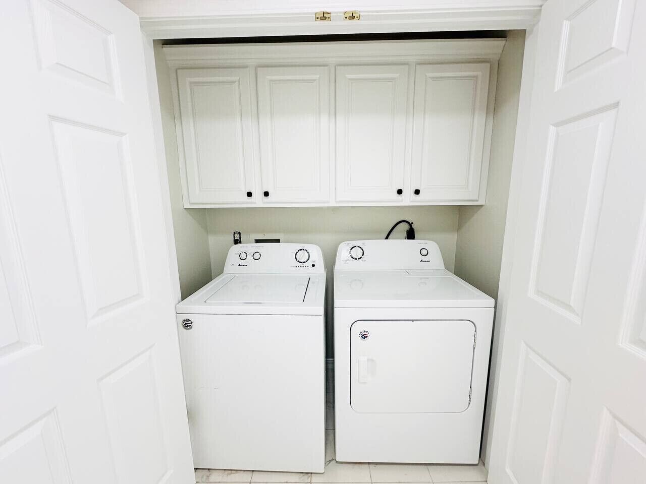 A laundry room with two white washing machines and cabinets above them.