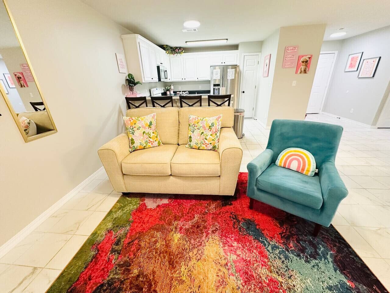 Een woonkamer met een beige bank, een blauwgroene fauteuil en een kleurrijk vloerkleed.