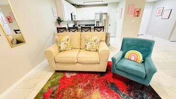 Een woonkamer met een beige bank, een blauwgroene fauteuil en een kleurrijk vloerkleed.