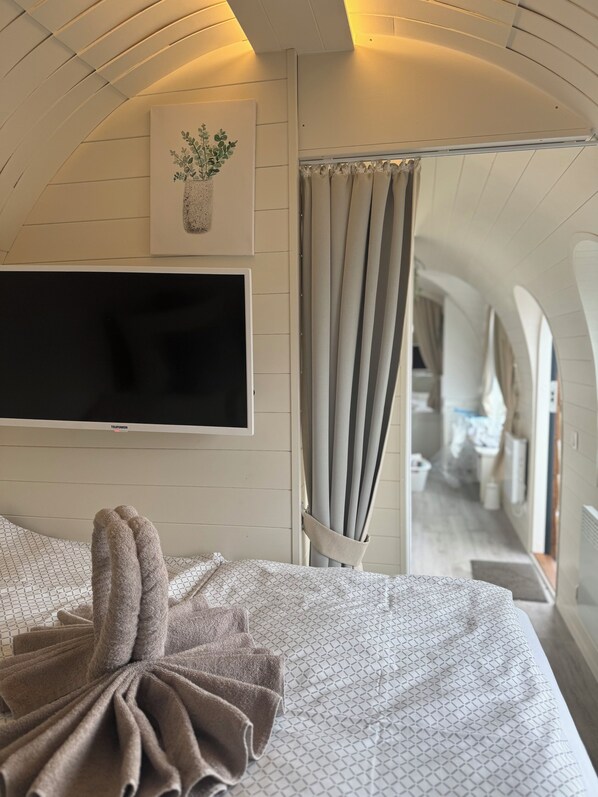 Une chambre moderne avec un lit, un téléviseur fixé au mur et une vue sur un couloir.