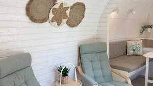 Een knus ingerichte kamer met twee groene fauteuils, een tafeltje met een plant en een bank met kussens.