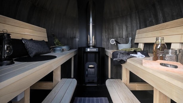 Een gezellige, gedimde kamer met een houtkachel, houten banken en diverse keukenspullen.