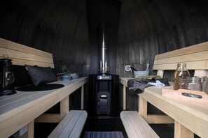 A cozy, dimly lit room with a wood-burning stove, wooden benches, and various kitchen items. - Iglu Camp Tangermünde (Tangermünde)