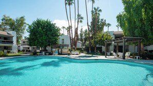 Una piscina con sillas de descanso y una pérgola, rodeada de palmeras y edificios.