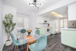 A modern kitchen with white cabinets, a dining area with teal chairs, and a potted plant. - Palm Canyon Retreat, 2bd 2ba with Pool and Patio (Palm Springs)