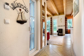 A hallway with a 'WILKOMMEN' sign, a sailboat decoration, a fireplace, and a dining area with a red tablecloth. - Holiday Home 'Am Hünengrab' with Shared Terrace (Lütow)