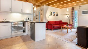 Eine Küche mit weißen Schränken und einem eingebauten Ofen, ein rotes Sofa, ein kleiner Tisch und ein schwarzer Schrank.