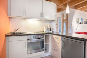 A kitchen with white cabinets, a built-in oven, a dishwasher, and a countertop with a kettle and coffee maker. - Holiday Home 'Am Hünengrab' with Shared Terrace (Lütow)