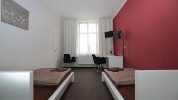 Una habitación con dos camas individuales, un escritorio, dos sillas, una ventana con cortinas y una pared de acento roja.