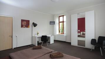 A hotel room with a bed, desk, chair, TV, and a red wall.
