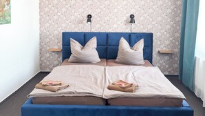 A double bed with a blue headboard, two bedside lamps, and a floral-patterned wall. - BEWOS Gästehaus (Oschersleben)