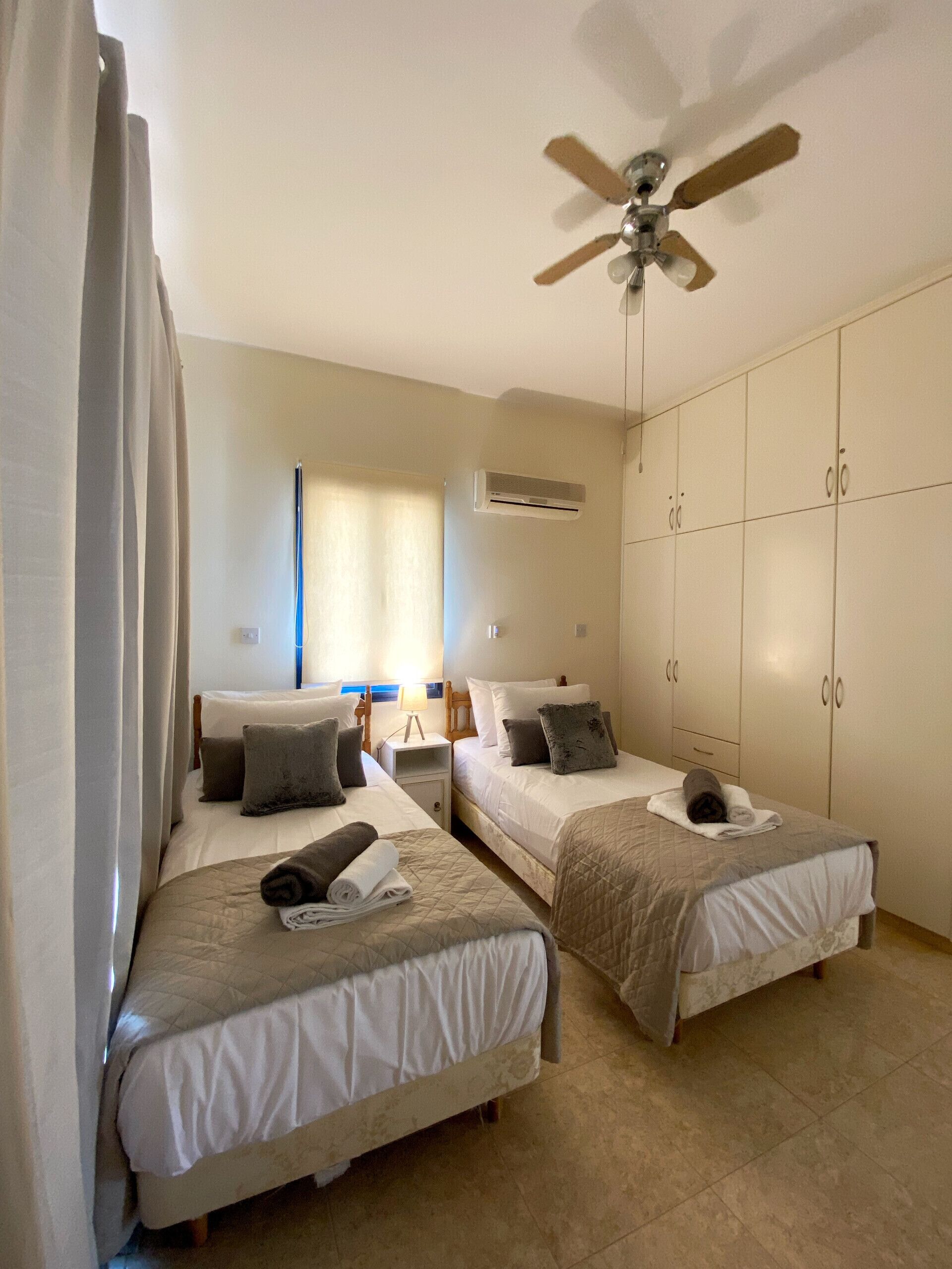 Une chambre d’hôtel avec deux lits, un ventilateur de plafond, un appareil de climatisation et une armoire.
