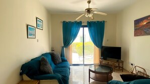 Ein Wohnzimmer mit einer Couch, einem Fernseher, einem Deckenventilator und Blick durch eine Glastür.