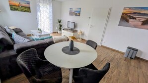 Una sala de estar con una mesa redonda, un sofá, un televisor y una puerta.