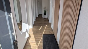 Un pasillo con suelo de madera, paredes blancas y un felpudo negro.