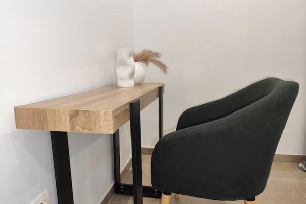 Escritorio de esquina con tapa de madera clara y patas de metal negro, acompañado por una silla tapizada en verde oscuro.
