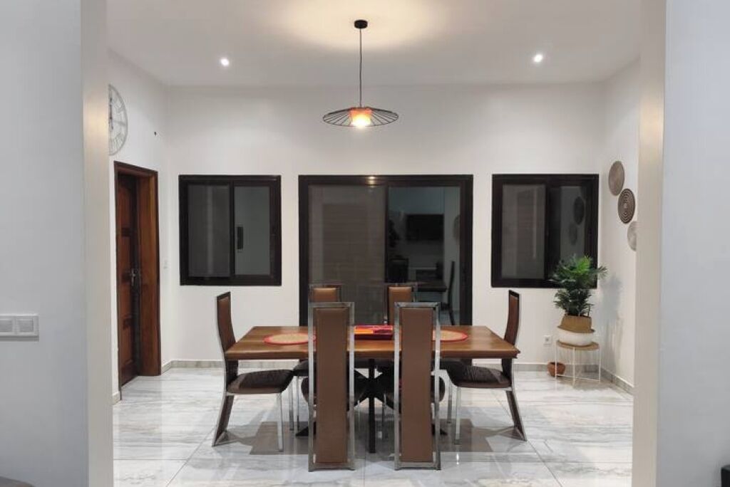 Un coin repas comprenant une table rectangulaire, quatre chaises, un luminaire suspendu et une plante en pot.