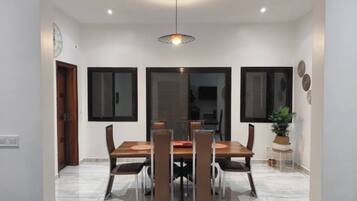 Un coin repas comprenant une table rectangulaire, quatre chaises, un luminaire suspendu et une plante en pot.