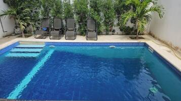 Une piscine à l’eau d’un bleu cristallin, entourée d’un petit muret et agrémentée de plusieurs chaises longues.