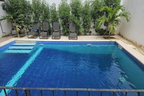 Une piscine à l’eau d’un bleu cristallin, entourée d’un petit muret et agrémentée de plusieurs chaises longues.
