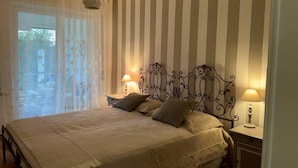 A bedroom with a bed, two bedside lamps, a window with sheer curtains, and a striped wall. - Garden view apartment in Sanremo with veranda (Sanremo)