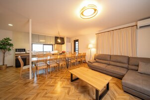 A modern living room with a wooden herringbone floor, a brown sofa, a wooden coffee table, and a dining area with wooden chairs and a table.