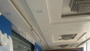 A spacious lobby with a marble floor, a glass wall with a cloud mural, and a reception area with a wooden door. - The Divine Cloud Inn (Aligarh)