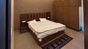 A bedroom with a bed, wooden wardrobe, ceiling fan, and recessed lighting. - The Divine Cloud Inn (Aligarh)