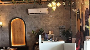 A modern interior with a reception desk, a large arched window, and a ceiling with hanging plants. - The Divine Cloud Inn (Aligarh)