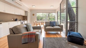 A modern living space with a kitchen, two sofas, a dining area, and large windows. - On The Bay: Sundrenched Stunner. Pet-friendly opposite beach. (Quindalup)
