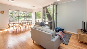 A spacious living room with a large window, a dining area, and a TV stand. - On The Bay: Sundrenched Stunner. Pet-friendly opposite beach. (Quindalup)