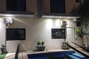 Uma área de piscina com design moderno, incluindo uma piscina pequena, plantas em vasos e unidades de ar condicionado fixadas na parede.