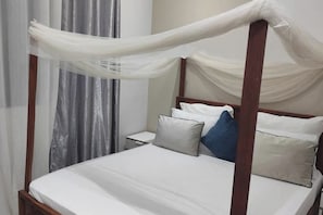 Uma cama com dossel, roupa de cama branca e cortinas.