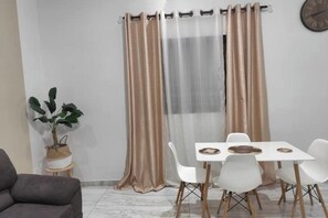 Um quarto com uma mesa de jantar posta para quatro pessoas, uma planta em vaso e um relógio na parede.