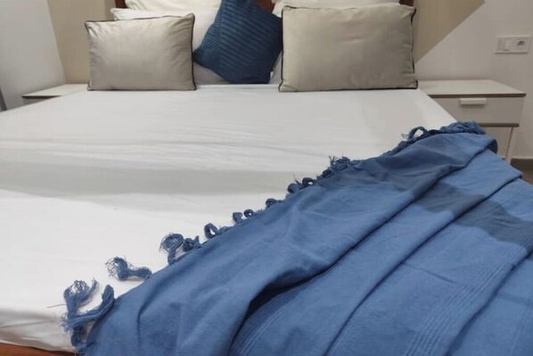 A bed with a white mattress and a blue blanket with frayed edges.