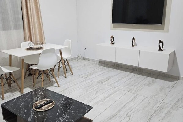 Ein modernes, minimalistisches Wohnzimmer mit einem weißen Esstisch, weißen Stühlen, einem schwarzen Marmorkaffeetisch und einer weißen Unterhaltungsanlage mit dekorativen Gegenständen.
