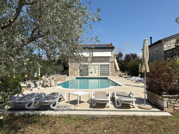 A pool area with lounge chairs, a stone building, and a clear sky.
